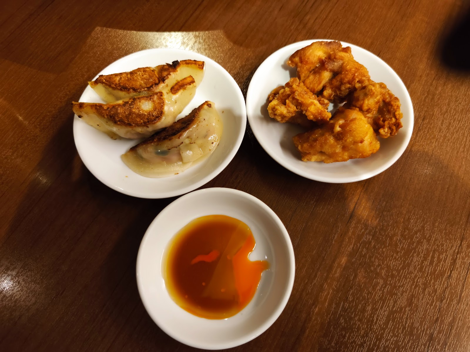 白い小皿に焼き餃子が三つ、隣の皿に唐揚げ、手前に辣油の入ったたれ皿。