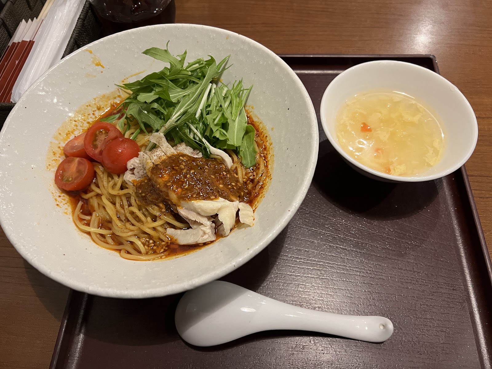 漆の盆に、棒々鶏のせ麺の鉢と卵スープ、白い蓮華。麺には蒸し鶏、水菜、ミニトマト、ごまだれ。